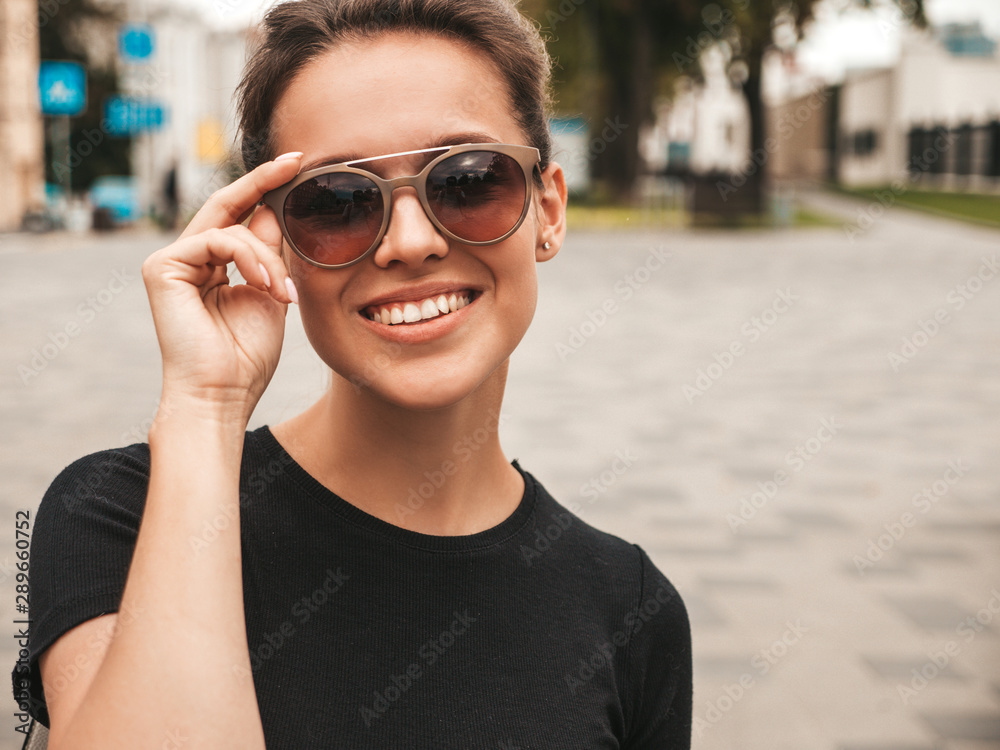 Portrait of beautiful smiling hipster model dressed in summer clothes. Trendy girl posing in the street background in sunglasses. Funny and positive woman having fun