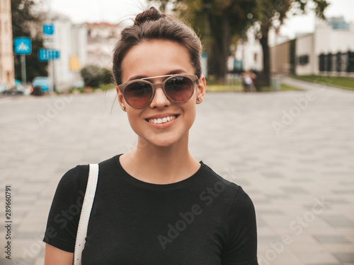 Portrait of beautiful smiling hipster model dressed in summer clothes. Trendy girl posing in the street background in sunglasses. Funny and positive woman having fun