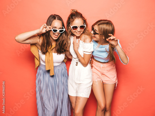 Three young beautiful smiling hipster girls in trendy summer clothes. Sexy carefree women posing near pink wall in studio. Positive models going crazy and having fun in sunglasses © halayalex