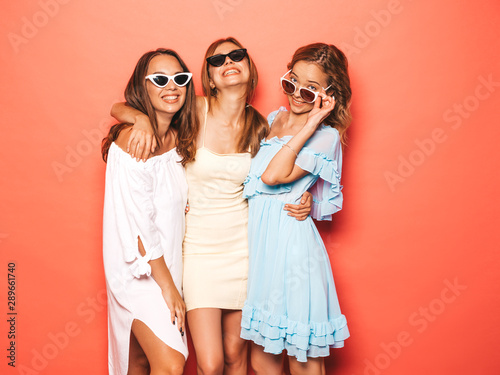 Three young beautiful smiling hipster girls in trendy summer clothes. Sexy carefree women posing near pink wall in studio. Positive models going crazy and having fun in sunglasses