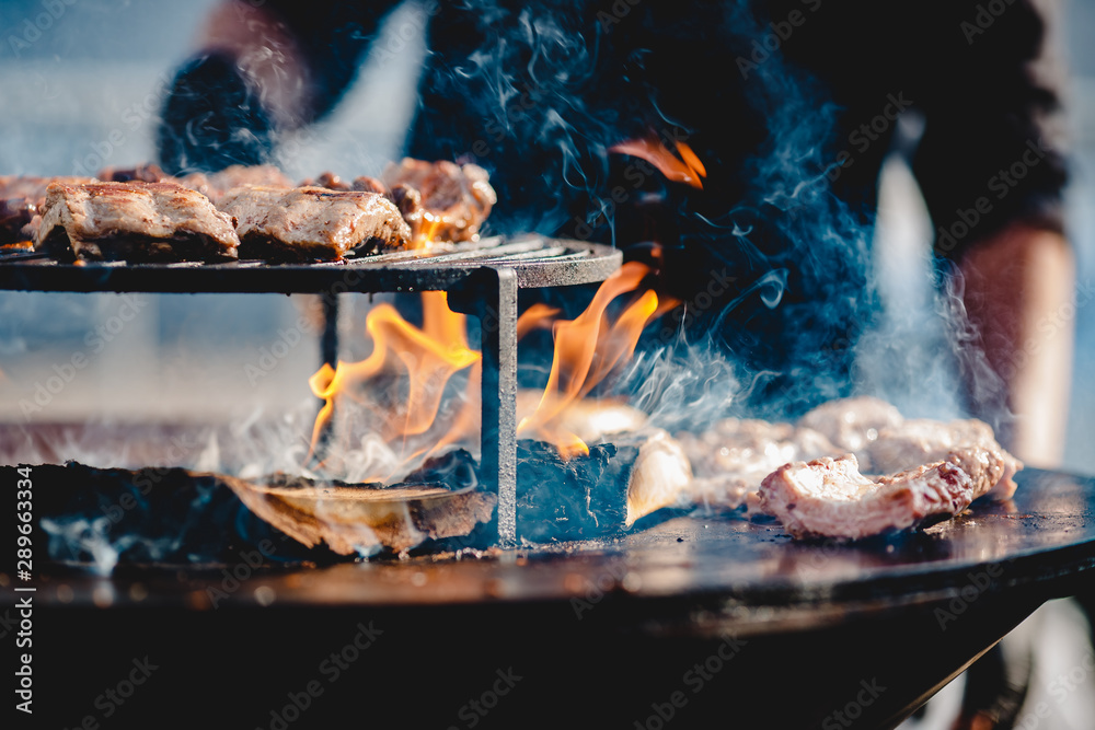 Cook grills steaks and pork ribs open fire. Turns meat over with tongs. Street food concept Cook grills steaks and pork ribs open fire. Turns meat over with tongs. Street food concept
