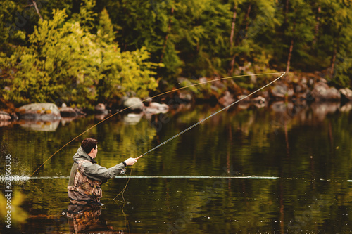 Fisherman using rod fly fishing in mountain river autumn splashing water