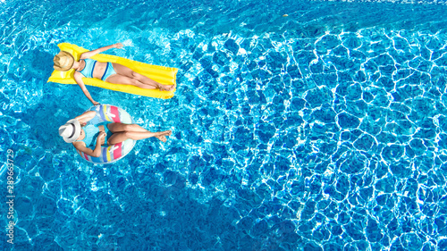 Children in swimming pool aerial drone view fom above, happy kids swim on inflatable ring donut and mattress, active girls have fun in water on family vacation on holiday resort