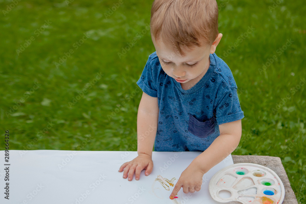 Cute little boy painting with a paint hands using gauche paints Cute little boy painting with a paint hands using gauche paints