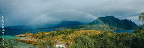 Panoramic photo of rainbow, sea, hills, blue sky in Norway on summer.