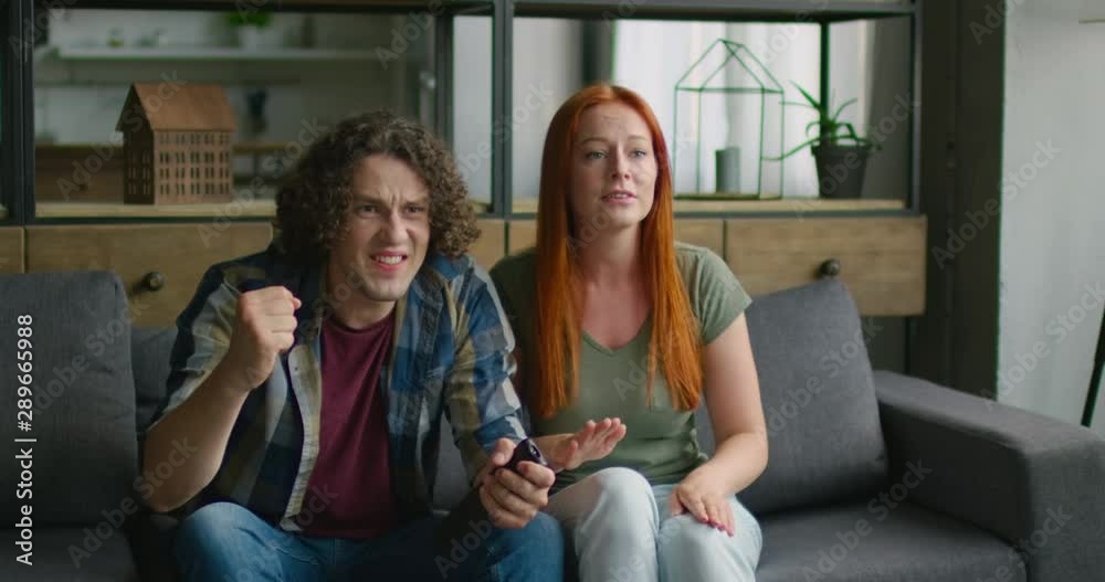 Young couple is celebrating a scored goal by their best sport team, sitting on a sofa at home, cheering, hugging each other, having great evening together, indoor. 4K, Middle plan, RED camera. Young couple is celebrating a scored goal by their best sport team, sitting on a sofa at home, cheering, hugging each other, having great evening together, indoor. 4K, Middle plan, RED camera.