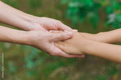 Closeup view of mother and baby holding hands outdoor. Horizontal color photography.