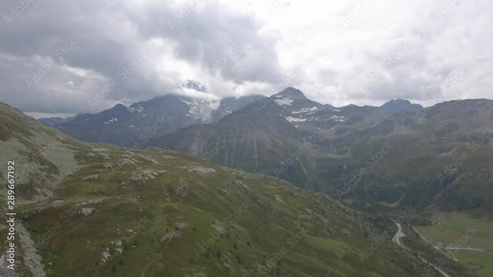 Drone flight over a high alpine mountain road pass. The drone fly`s over the barren mountain terrain. The clouds form over the background mountains in a spectacular alpine valley. Drone flight over a high alpine mountain road pass. The drone fly`s over the barren mountain terrain. The clouds form over the background mountains in a spectacular alpine valley.