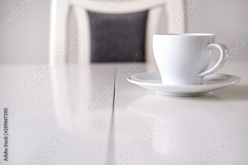 Konzept Warten, GesprÃ¤ch oder Meeting: Blick auf eine weiÃŸe Kaffeetasse an einem weiÃŸen Tisch mit Stuhl â€“ selektiver Fokus mit sehr TiefenunschÃ¤rfe