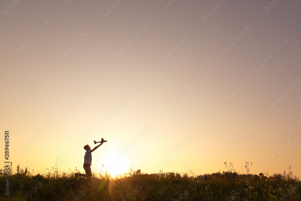 Cute white kid playing happily outdoor with big toy plane during gold sunset time in summer landscape. Horizontal color photography.