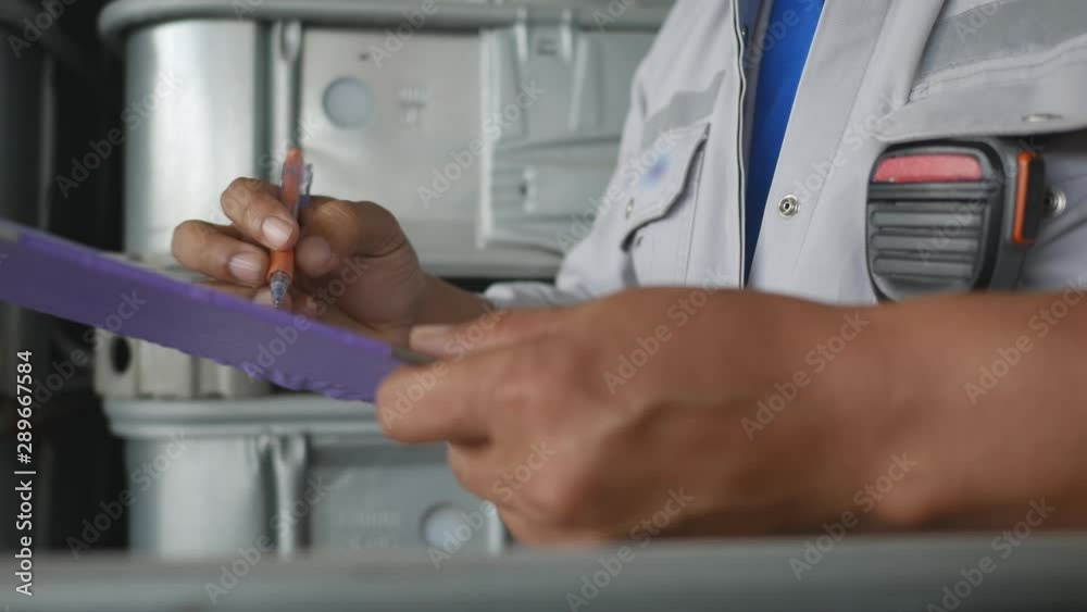 A man to check quantity and quality of chemical tank in warehouse and record to check sheet on clipboard