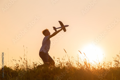 Cute white kid playing happily outdoor with big toy plane during gold sunset time in summer landscape. Horizontal color photography. © Andrii Oleksiienko