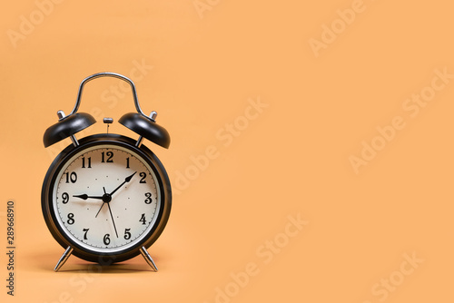 Black alarm clock on orange pastel background