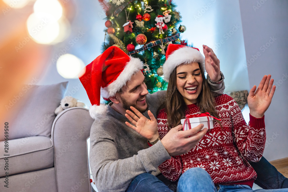 happy couple in stylish sweaters holding gift with bow in festive room at christmas tree. happy couple in stylish sweaters holding gift with bow in festive room at christmas tree.