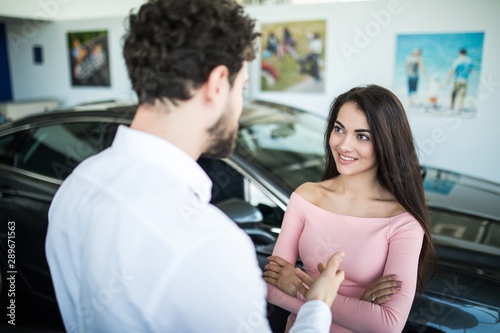 Successful young lady discussing her potential purchase with a car dealer in showroom