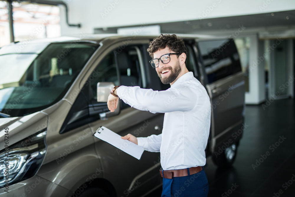 Handsome car dealership worker smiling while standing near the car Handsome car dealership worker smiling while standing near the car