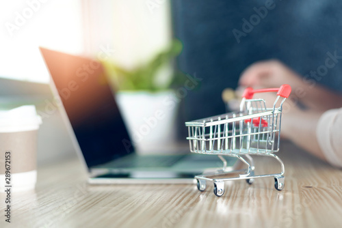 Red shopping cart on a laptop keyboard near the window at home.Easy shopping with finger tips for consumers.Online shopping concept.