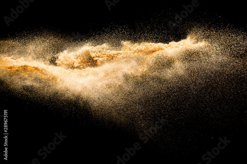 Dry river sand explosion. Golden colored sand splash against black background.