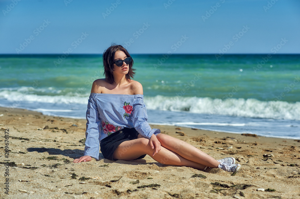 Beautiful young healthy girl in fashionable sunglasses at the seaside . The model wears a blouse and skirt