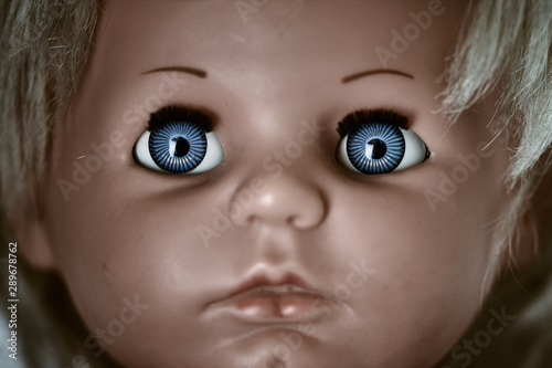 Creepy and dark doll's head. A scary face of a blonde baby vintage doll with blue eyes