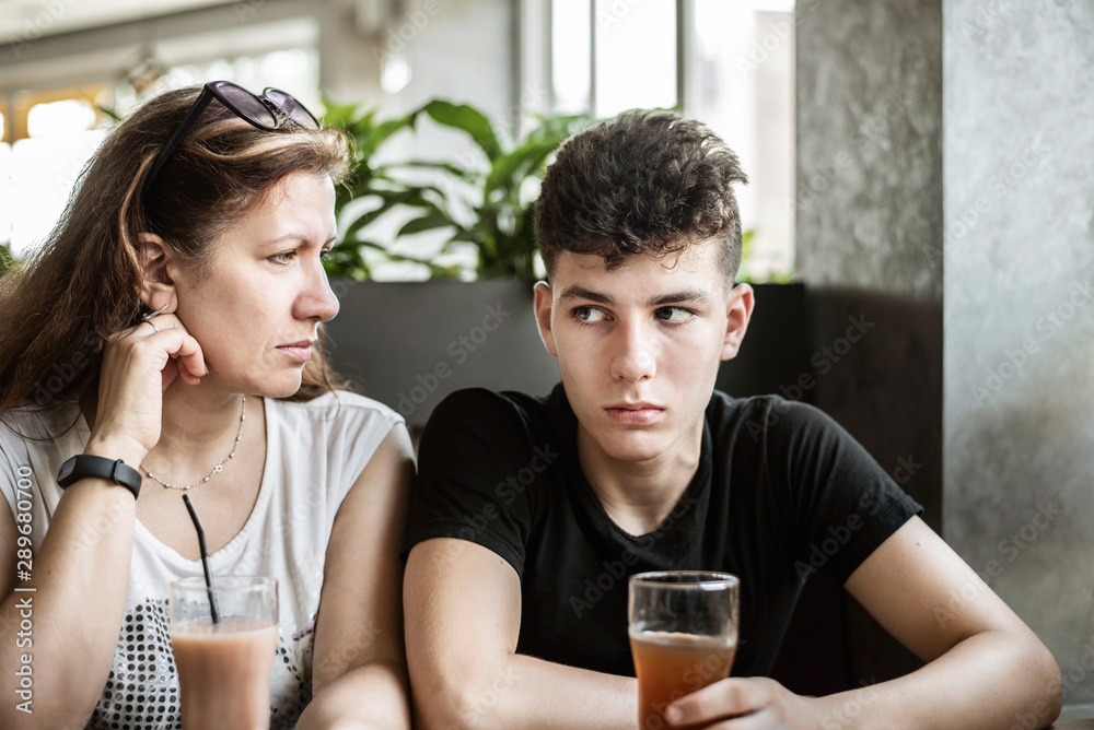 Woman with her teenage son sit in a cafe and drink juice, they have sad, serious faces, they try to reconcile after quarrel. The boy has a difficult character