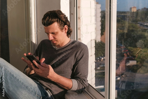 Man looks at mobile phone, flipping the tape in social networks sitting on the balcony at sunset