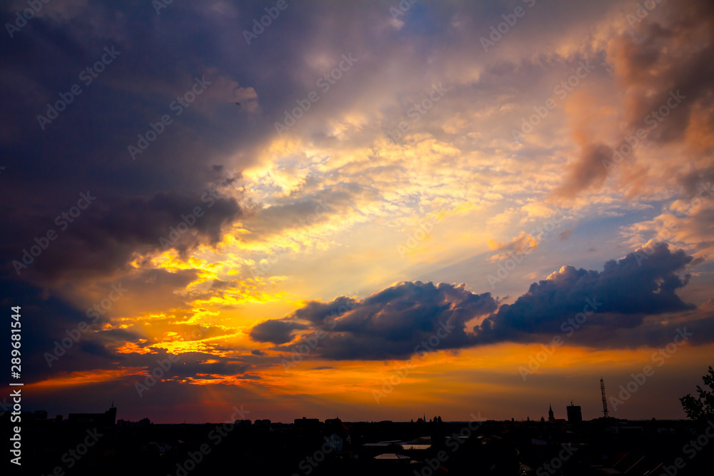 Silhouette of city under dark sky with cumulus clouds at sunset