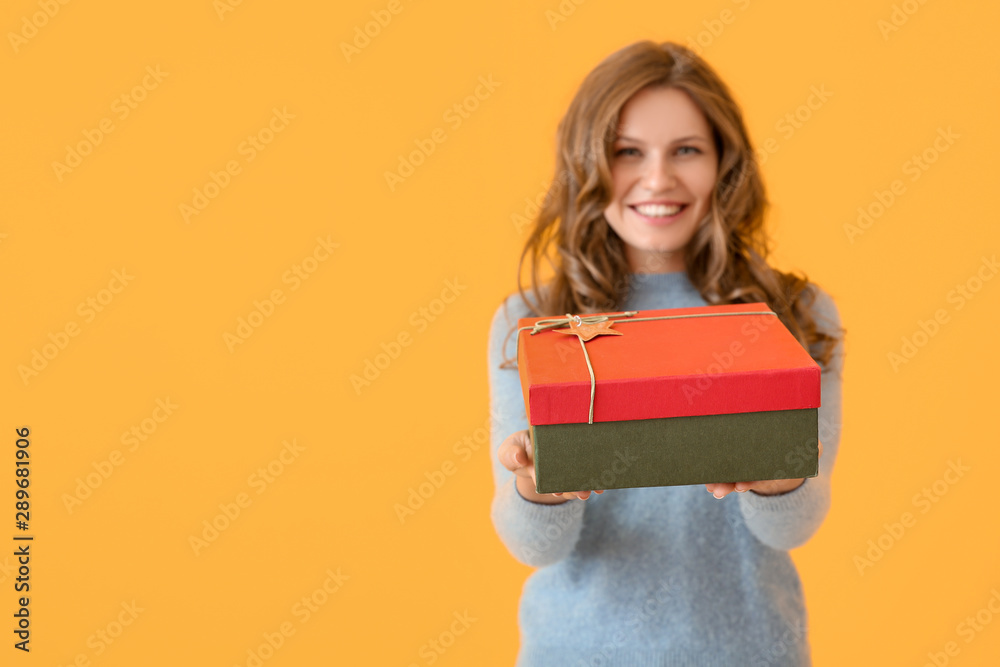 Happy young woman with Christmas gift on color background