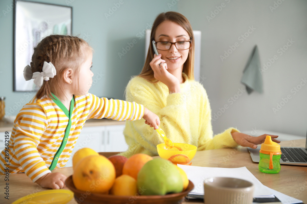 Little daughter with working mother in kitchen at home Little daughter with working mother in kitchen at home