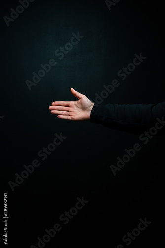 Isolated man's right hand, reaching out for a handshake, on a black background, wearing a hoodie.