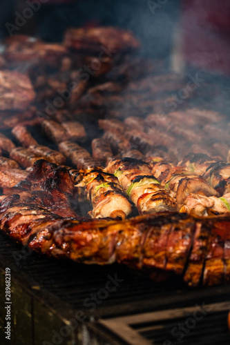 Juicy steaming meat on a charcoal grill, pork steaks, chicken breast, sausages, pieces of meat chops at a street food festival