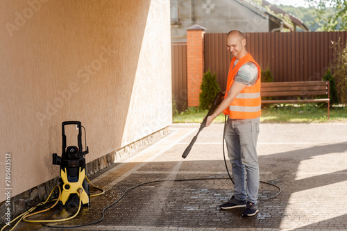 A man in an orange vest cleans a tile of grass in his yard near the house. High pressure cleaning