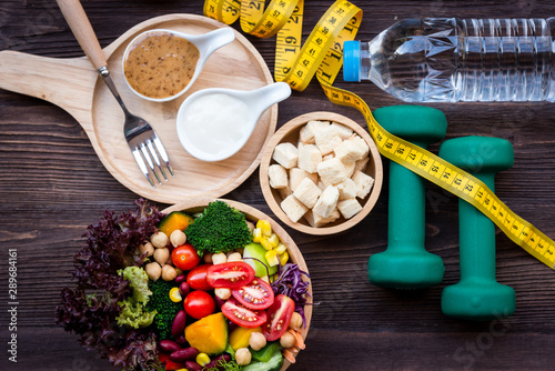 Fresh vegetable salad and healthy food for sport equipment for women diet slimming with measure tap for weight loss on wood background. Healthy Sport Concept