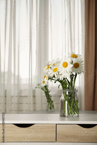 Vase with beautiful chamomile flowers on cabinet in room. Space for text