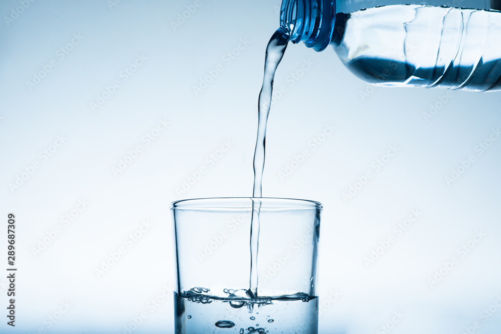 Pouring water from bottle into glass against grey background. Refreshing drink Pouring water from bottle into glass against grey background. Refreshing drink