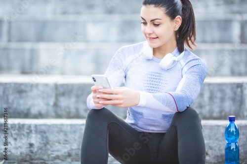 Young woman after training checks sport tracker. Fitness concept outfit thermal underwear headphones and smartphone