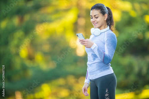 Young woman after training checks sport tracker. Fitness concept outfit thermal underwear headphones and smartphone