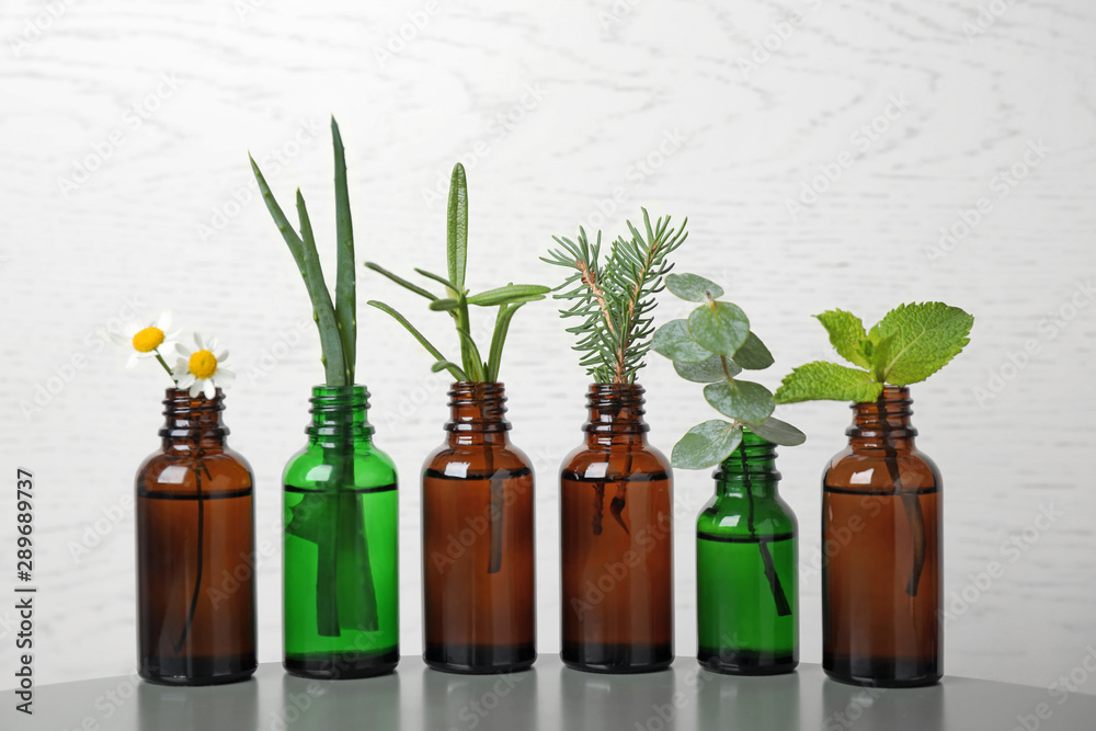 Glass bottles of different essential oils with plants on table Glass bottles of different essential oils with plants on table