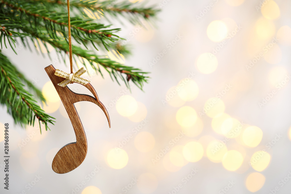 Fir tree branch with wooden note against blurred lights, space for text. Christmas music