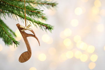 Fir tree branch with wooden note against blurred lights, space for text. Christmas music
