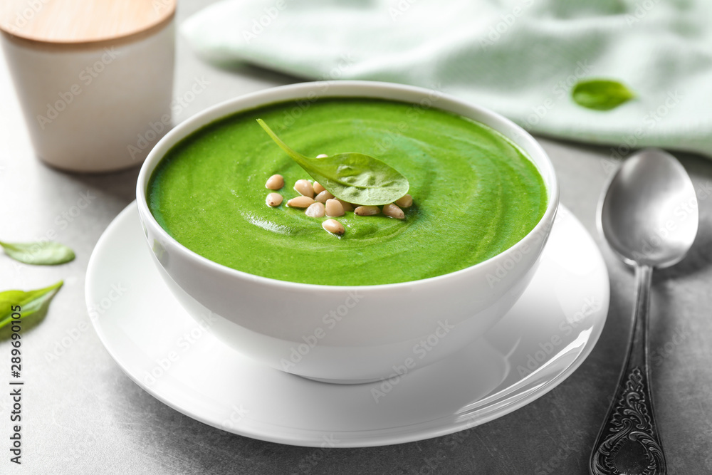 Bowl of healthy green soup with fresh spinach on grey table Bowl of healthy green soup with fresh spinach on grey table