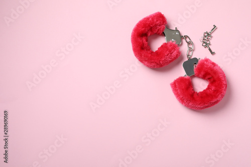 Red furry handcuffs and keys on pink background, top view with space for text. Sex toy