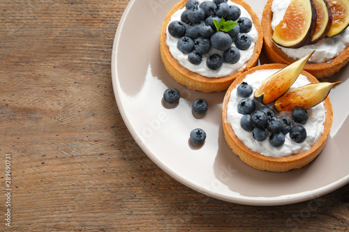 Tarts with blueberries and figs served on wooden table, top view with space for text. Delicious pastries