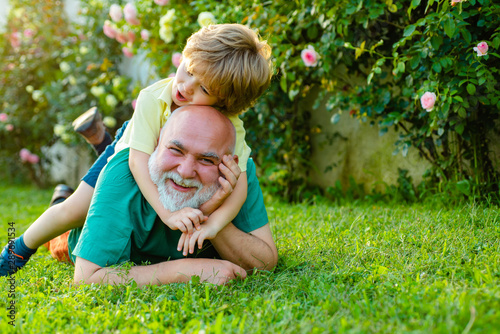Grandfather and son. Family summer and active holidays. Happy senior man Grandfather with cute little boy grandson playing and looking at camera. Cute child boy hugging his grandfather.
