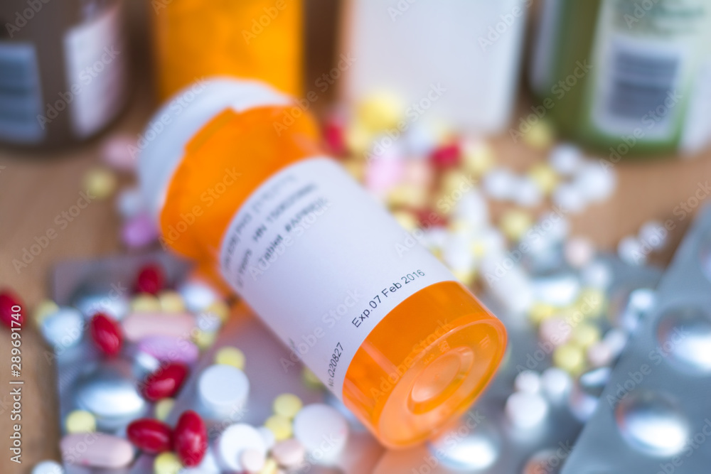 Pile of various expired prescription medicines and bottle focused on