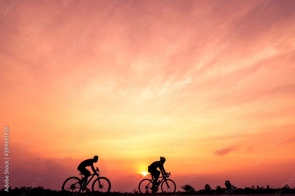 Obraz premium Silhouette of cyclists ride bicycle on sunset background. Two men Ride on bike on the road, Sport and active life concept