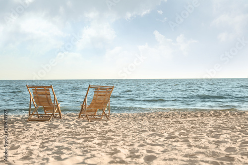 Wooden deck chairs on sandy beach near sea © New Africa