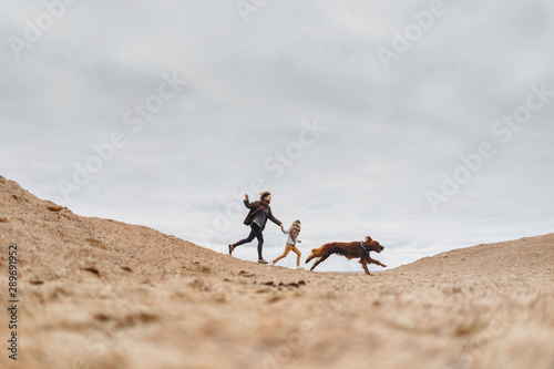 Happy family and their dog running along the sandy beach