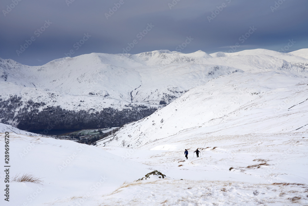 Two hikers ascending the snowy mountain summit of Rampsgill Head from The Knott near Hartsop.