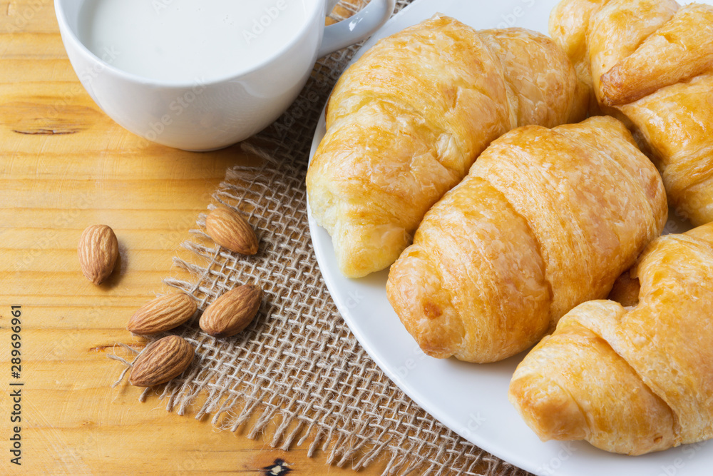 Closeup croissant with almond and milk on wooden table. breakfast concept.